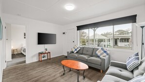 A modern living room with a grey sofa, a wooden coffee table, and a flat-screen TV mounted on the wall. - Phillip Island Cottage 1 (Cowes)