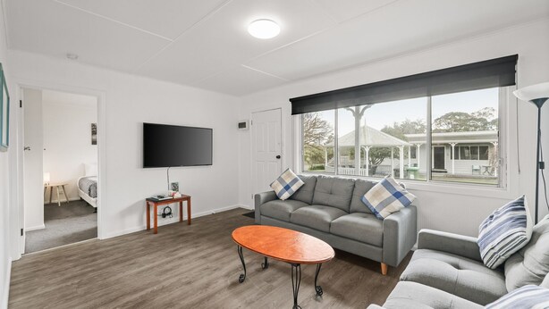 Un salon moderne avec un canapé gris, une table basse en bois et un téléviseur à écran plat fixé au mur.