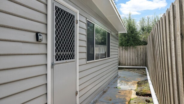 A residential building with a metal security gate, a concrete pathway, and a wooden fence. - Phillip Island Cottage 4 (Cowes)