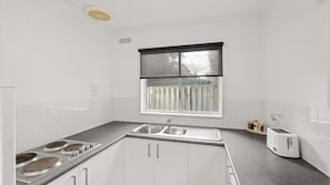 A compact kitchen with a built-in gas stove, a double sink, and a window above the sink. - Phillip Island Cottage 4 (Cowes)