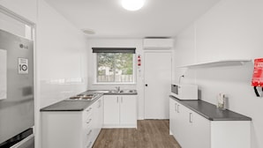 A compact kitchen with white cabinets, a stainless steel sink, a microwave, and a window with a view of the outside. - Phillip Island Cottage 5 (Cowes)
