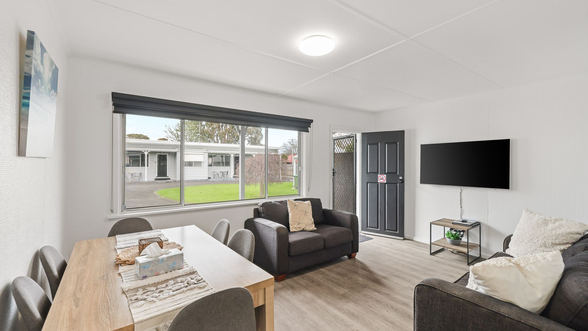 A modern living room with a dining area, a sofa, a TV, and a view of the outside.