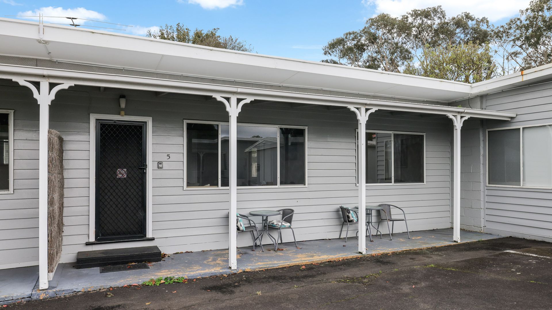 A motel with a covered porch, a black door, and two tables with chairs.