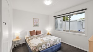 A bedroom with a bed, two bedside tables, a window, and a door. - Phillip Island Cottage 5 (Cowes)