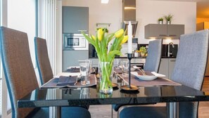 A dining table with chairs, a vase with flowers, and a kitchen in the background. - Holiday Apartment With 1 Bedroom (Heiligenhafen)
