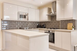 A modern kitchen with a central island, stainless steel appliances, and a tiled backsplash. - 3BR Flat in Bromley |Near Local Stores & Resto | ST (London)