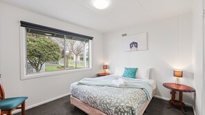 A hotel room with a large window, a bed with floral bedding, two bedside tables with lamps, and a framed picture on the wall.