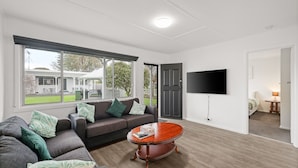 A modern living room with a sofa, a coffee table, and a TV mounted on the wall. - Phillip Island Cottage 6 (Cowes)
