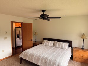 A bedroom with a bed, a ceiling fan, a nightstand with a lamp, and a wooden door. - Cozy 2 bedroom condo in amazing Mount Hood Village with AC on the golf course. (Mount Hood Village)