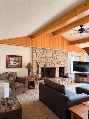 A living room with a stone fireplace, wooden beams, a television, and a sofa. - Cozy 2 bedroom condo in amazing Mount Hood Village with AC on the golf course. (Mount Hood Village)