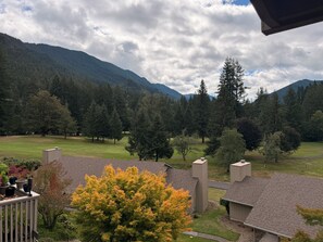 Un quartier résidentiel avec des maisons, un champ d’herbe et une montagne boisée en arrière-plan.