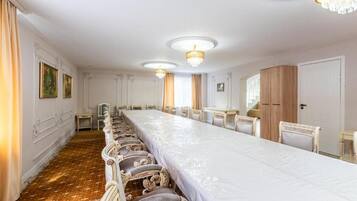 Una larga mesa de banquete con sillas, una araña y un armario de madera.