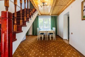 A staircase with wooden balusters leading to a room with a patterned carpet, a dining table with chairs, and a window with green curtains. - Tau Shyraq (Almaty)