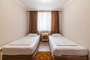 A hotel room with two single beds, a small table, and a window with curtains.