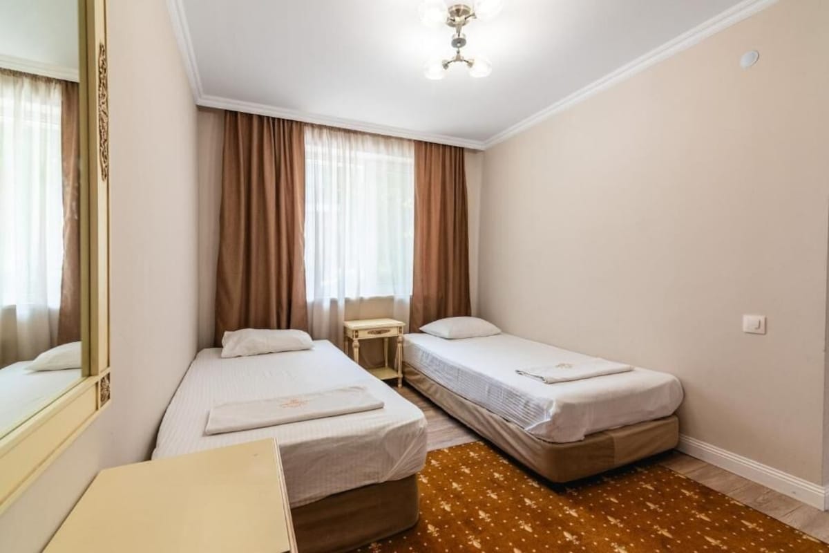 A hotel room with two beds, a bedside table, a mirror, and a ceiling light fixture.