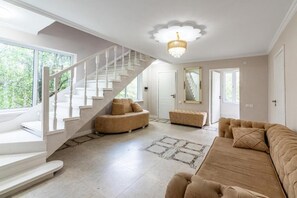 A spacious living area with a white staircase, a chandelier, and a beige sofa. - Tau Shyraq (Almaty)