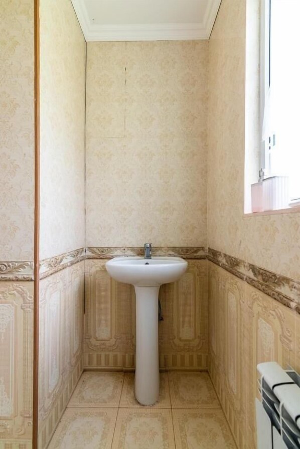 A bathroom with a pedestal sink, patterned walls, and a window.