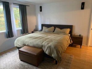 A bedroom with a bed, a nightstand, a bench, a window with curtains, and a wall-mounted light fixture.