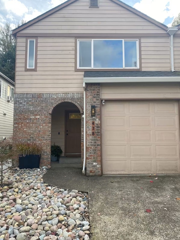 A two-story house with a garage, a brick entrance, and a gravel driveway.