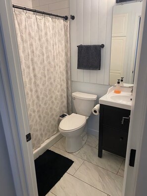 Een badkamer met toilet, douchegordijn, handdoekhouder en een wastafel met spiegel.