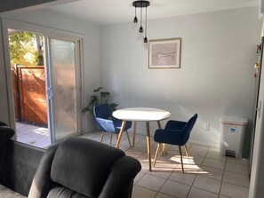 A modern living room with a sliding glass door leading to a patio, a round dining table with two chairs, and a framed picture on the wall.