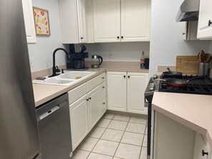 A compact kitchen with white cabinets, a dishwasher, a stove, and a coffee maker.