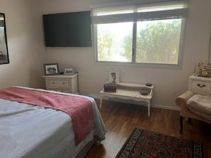 Een slaapkamer met een bed, nachtkastjes, een televisie en een raam met zonwering.