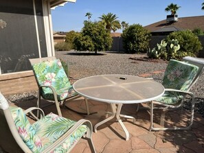 Een terras buiten met een ronde tafel en vier stoelen met bloemenmotieven.