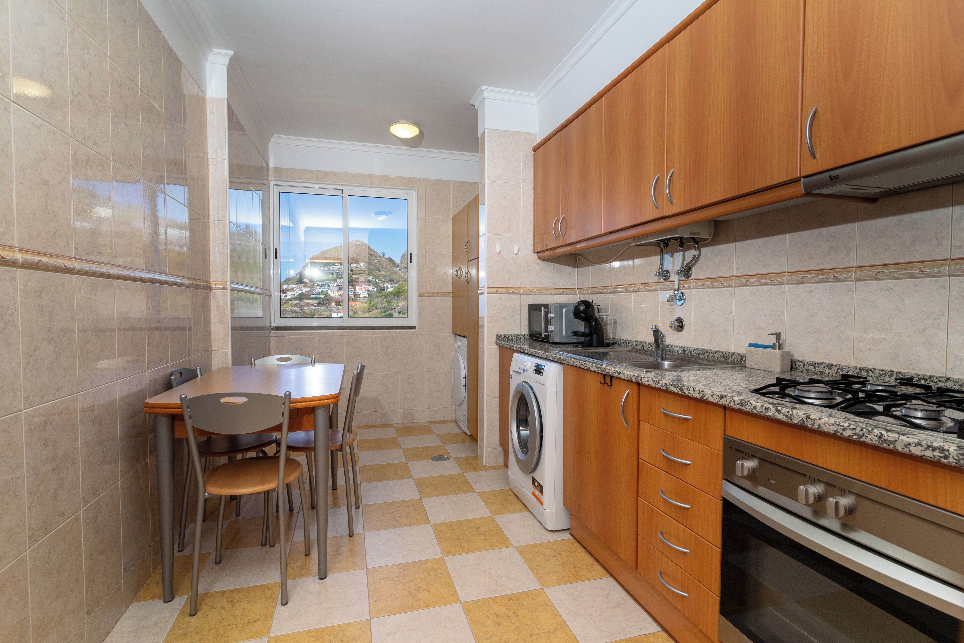 Una cocina con mesa, sillas, lavadora, estufa y armarios.