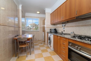 A kitchen with a dining table, chairs, a washing machine, a stove, and cabinets. - Lobos View (Câmara de Lobos)