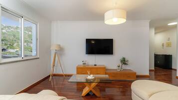 Ein modernes Wohnzimmer mit einem an der Wand befestigten Flachbildfernseher, einem Holztisch, einer Couch und einer Lampe.