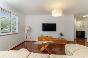 Ett modernt vardagsrum med en platt-TV som är monterad på väggen, ett soffbord i trä, en soffa och en lampa.
