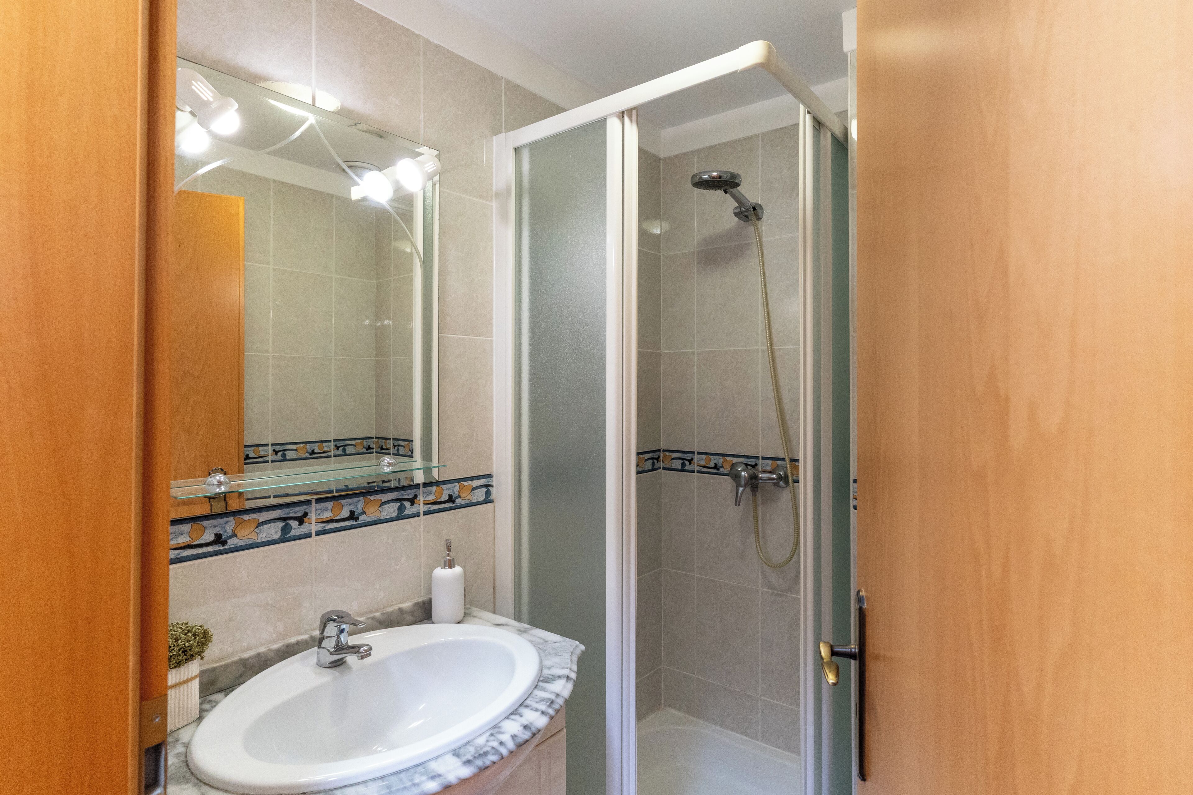 Un baño con ducha de vidrio, lavamanos con encimera de mármol y espejo con iluminación superior.