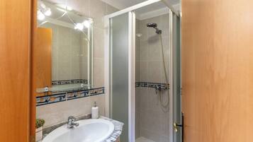 Un baño con ducha de vidrio, lavamanos con encimera de mármol y espejo con iluminación superior.