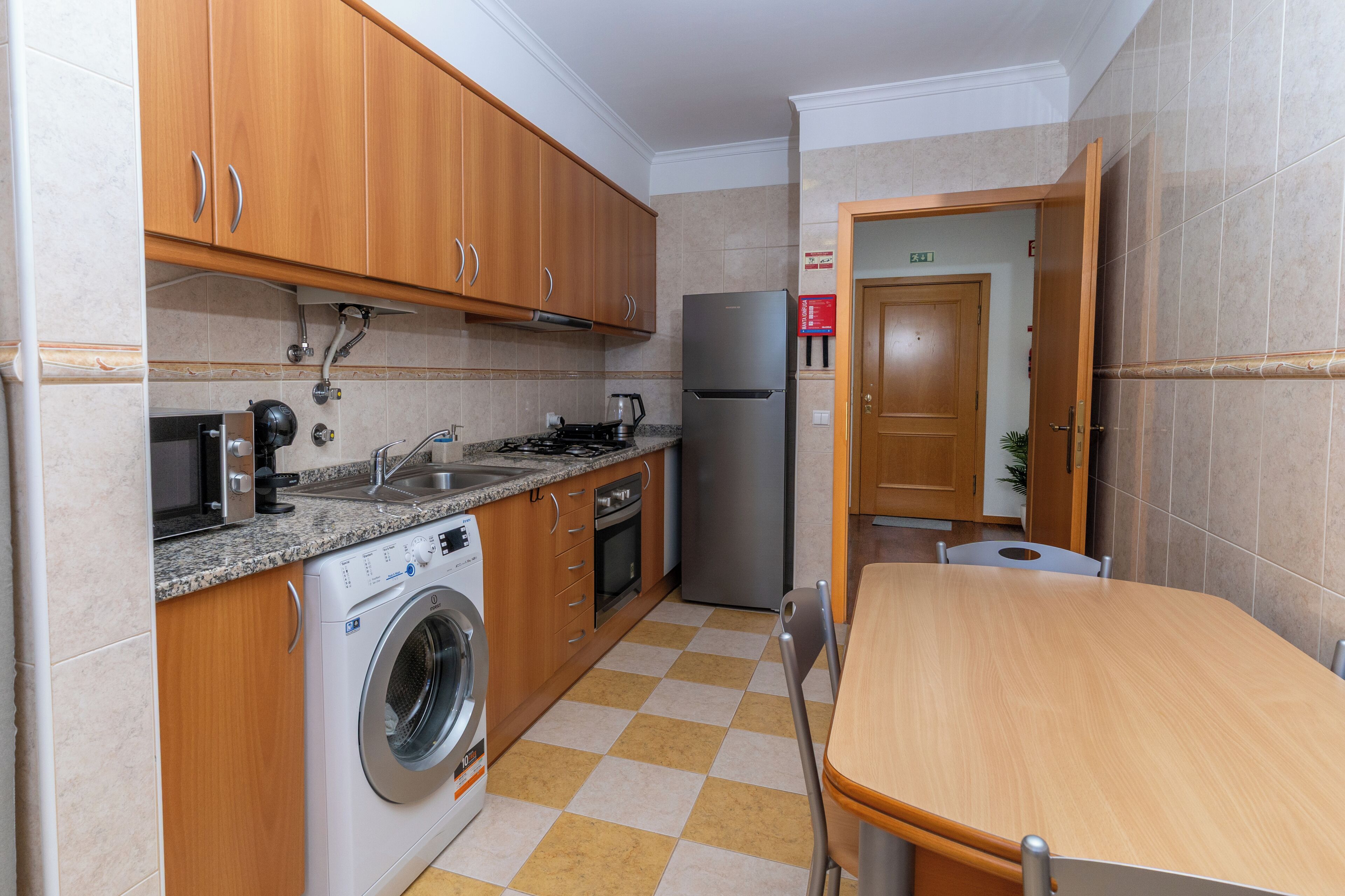 Eine kompakte Küche mit Holzausstattung, einer Waschmaschine, einem Kühlschrank und einer Essecke mit Tisch und Stühlen.