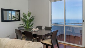 A dining area with a table and chairs, a potted plant, and a view of the ocean through a sliding glass door. - Vrbo Property (Câmara de Lobos)