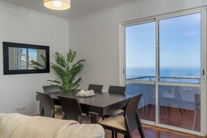 En matplats med ett bord och stolar, en krukväxt och utsikt över havet genom en skjutdörr i glas.