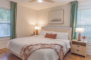 Een slaapkamer met een bed, nachtkastjes, een plafondventilator en een raam met gordijnen.