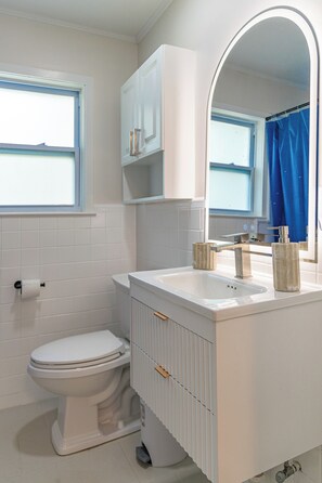 Een badkamer met een toilet, een wastafel, een spiegel en een raam.