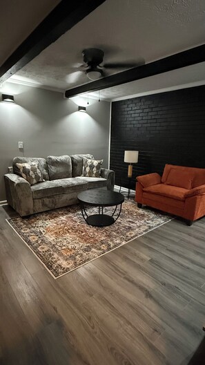 A living room with a sofa, a coffee table, and a red armchair. - The Cove #4. Rare find. Comfy 2Bedroom apartment in soothing Rockingham with AC. (Rockingham)