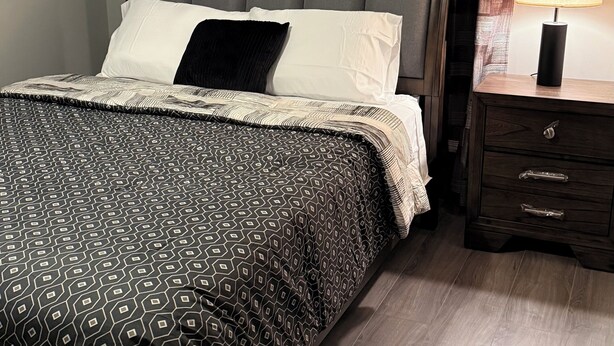 A bedroom with a bed, a nightstand, a lamp, and curtains. - The Cove #4. Rare find. Comfy 2Bedroom apartment in soothing Rockingham with AC. (Rockingham)