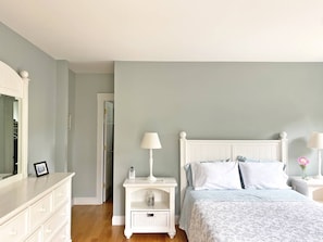 Un dormitorio con cama, mesitas de noche, cómoda y espejo.