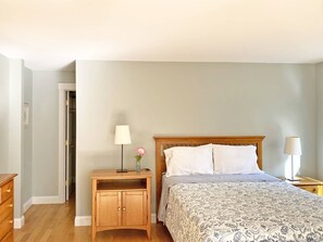 A bedroom with a wooden bed, two bedside tables with lamps, a nightstand, and a door leading to a closet. - Family Friendly Hidden Oaks Home (Oak Bluffs)