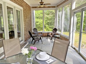 Un patio cubierto con una mesa preparada para dos, sillas y un jarrón con flores.