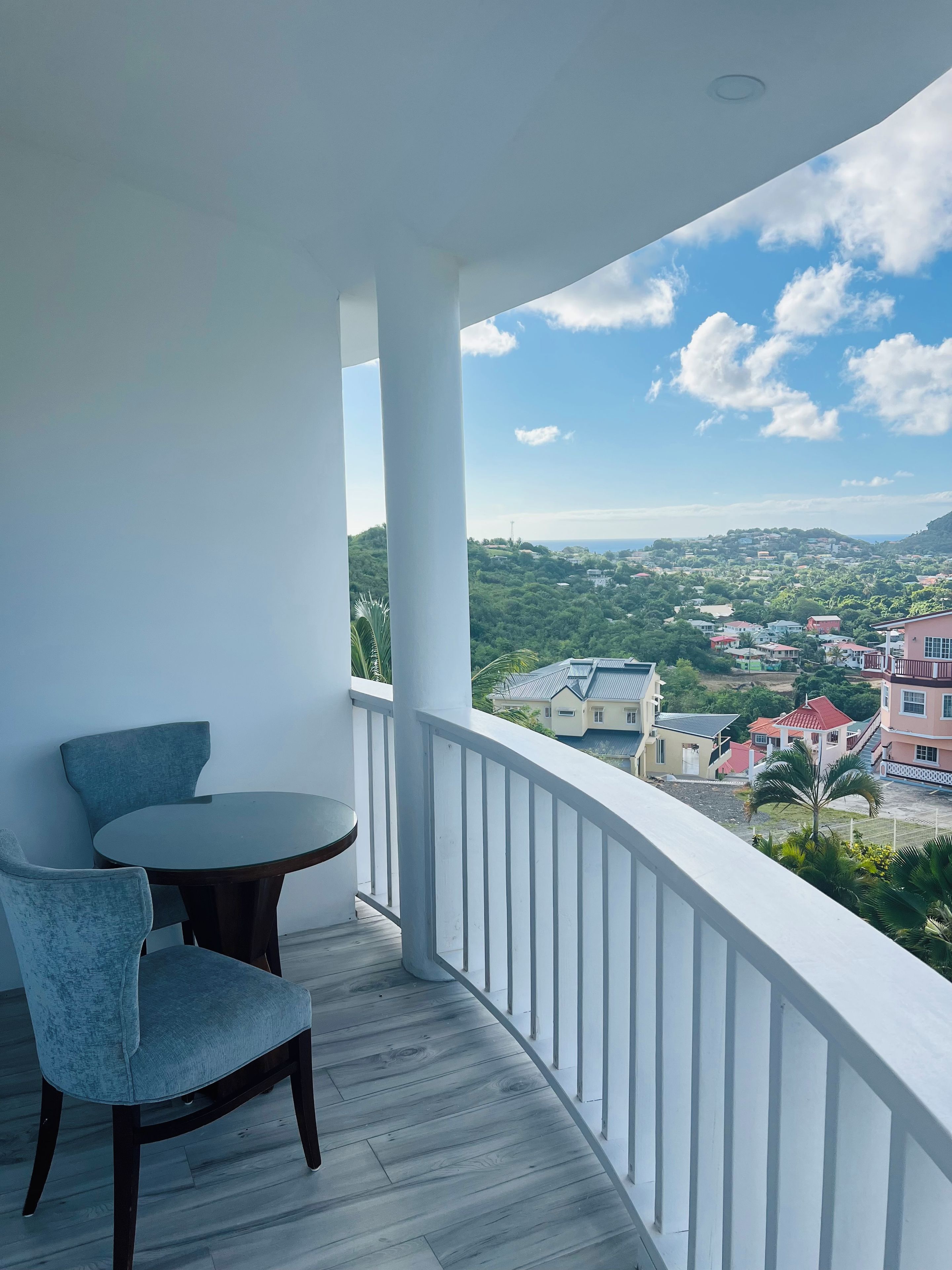 Un balcón con una mesa redonda y dos sillas, con vistas a una zona residencial con casas y vegetación.