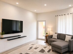 Een moderne woonkamer met een flatscreen televisie, een grijze bank, een kamerbreed tapijt met dessin en een bijzettafeltje met lamp.