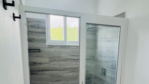 Une salle de bain avec une douche à parois de verre, des toilettes et une fenêtre.