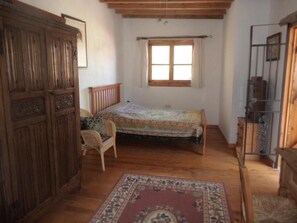 A bedroom with a wooden bed, a chair, a wardrobe, and a window. - Lantana Stone House.
Where the wild thyme scents the stone. (Lemona)