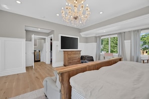 A bedroom with a large bed, a wooden dresser, a television, and a chandelier.