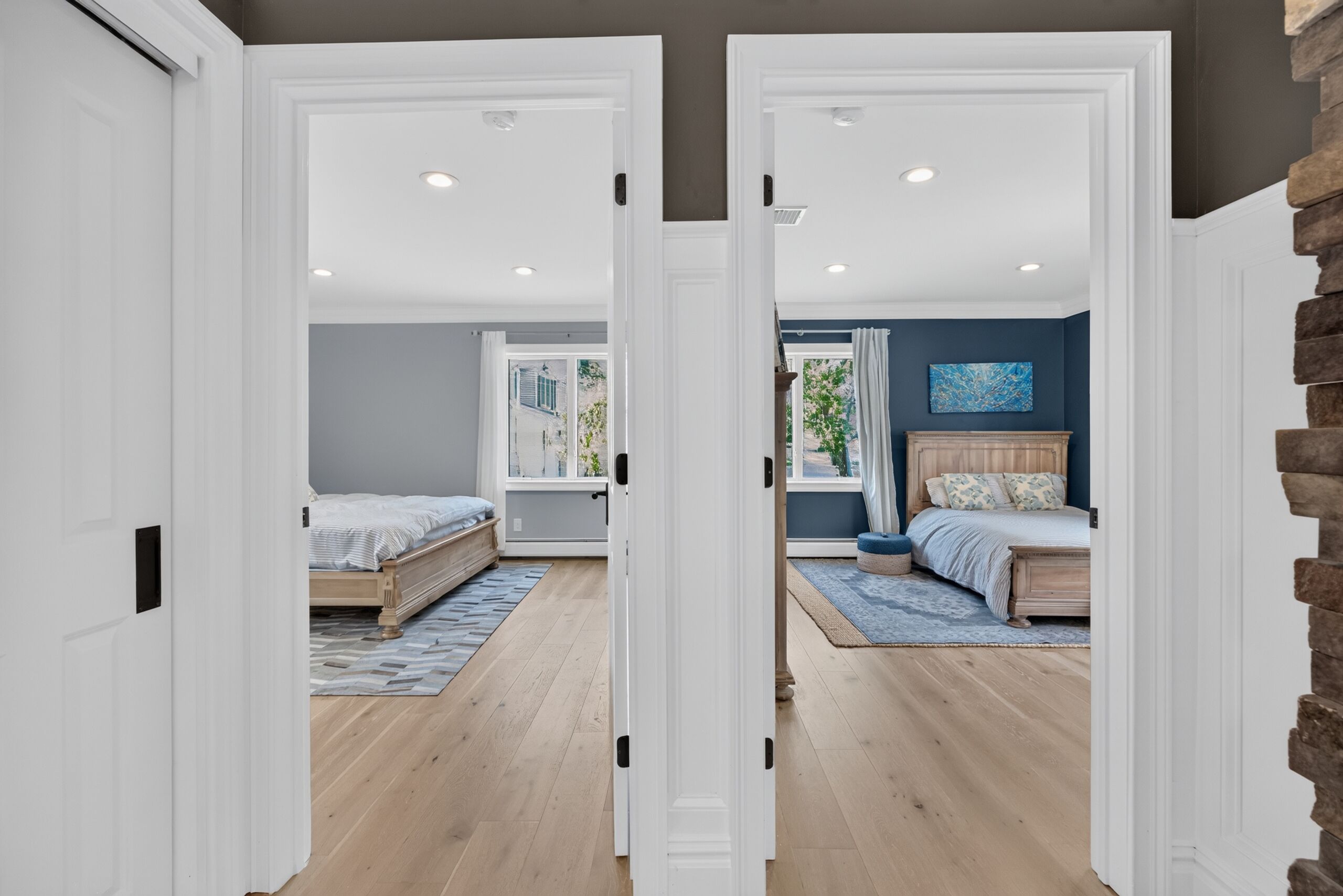 Un pasillo que conduce a dos dormitorios con piso de madera, una ventana y una pared de acento azul.